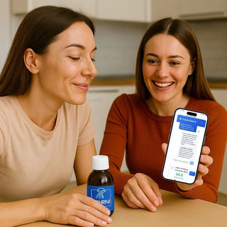 Deux femmes souriantes découvrent les conseils personnalisés du Coach Dohrnii sur smartphone, avec un flacon de phycocyanine posé sur la table – solution naturelle pour retrouver énergie et équilibre.