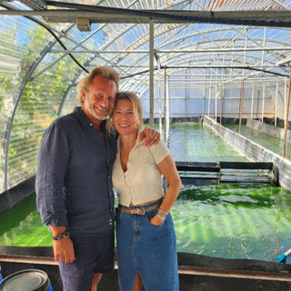 Les fondateurs de Dohrnii, Véro et Jeff souriants. Ils sont bronzés et habillés d'été. Jeff tient Véronique par l'épaule et sa joue contre ses cheveux. Derrière eux un bassin de culture de spiruline que l'on devine être le lien de leur production
