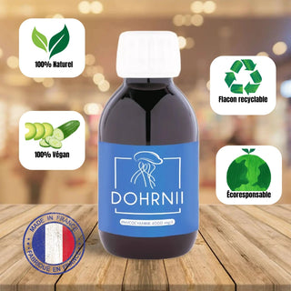 Flacon de phycocyanine Dohrnii posée sur une table en bois avec les garanties importantes du produit inscrite autour du flacon sur des étiquettes blanches - flacon recyclable - 100% naturel - 100% végan - Ecoresponsable - Fabriquée en France