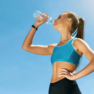 Femme sportive buvant de l’eau sous un ciel bleu – Hydratation, équilibre électrolytique et solutions naturelles contre la rétention d’eau."