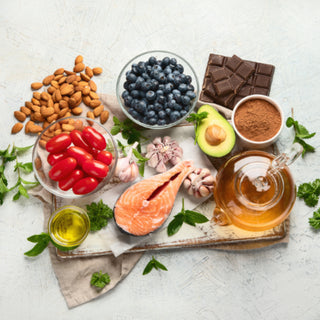 aliments antioxydants disposé sur une nappe : amandes, myrtilles, chocolat noir, cacao, avocat, ail, miel, saumon, huile d'olive, tomates cerise, persil