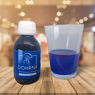 Phycocyanine Dohrnii posé sur une table à côté d'un verre rempli au tiers du produit. La couleur est d'un bleu profond